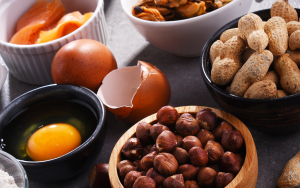 Assorted ingredients for cooking, including eggs, hazelnuts, peanuts, and smoked salmon, arranged on a gray countertop.